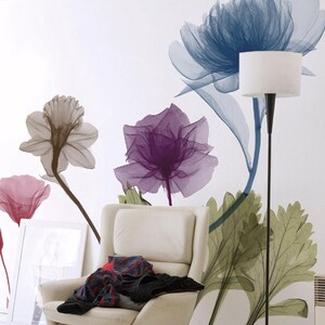May include: A wall mural featuring large, translucent, X-ray style floral illustrations in shades of blue, purple, pink, and grey. The mural is displayed on a white wall behind a cream-colored swivel armchair with a pile of clothing on the seat.