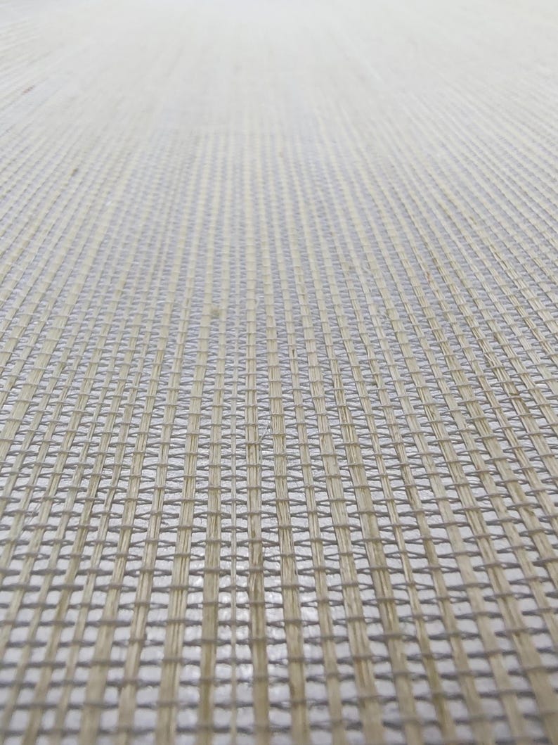Op de afbeelding: Een geweven materiaal met een lichtbeige en gebroken wit ruitpatroon. De textuur bestaat uit dunne, kruisende vezels die een consistente, herhalende vierkante weefstructuur vormen die over het gehele oppervlak uniform oogt.