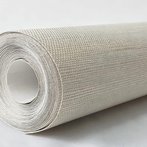 Op de afbeelding: Een rol gebroken wit behang met een subtiel, fijnkorrelig gestructureerd oppervlak. Het materiaal is strak opgerold in een cilindrische vorm en vertoont een consistente neutrale kleur en een geweven patroon over het gehele buitenoppervlak.
