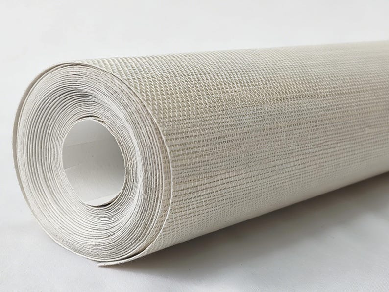 Op de afbeelding: Een rol gebroken wit behang met een subtiel, fijnkorrelig gestructureerd oppervlak. Het materiaal is strak opgerold in een cilindrische vorm en vertoont een consistente neutrale kleur en een geweven patroon over het gehele buitenoppervlak.