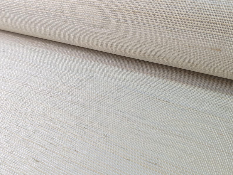 Op de afbeelding: Een rol gebroken wit textiel met een duidelijke horizontale slub-textuur. Het materiaal vertoont een geweven uiterlijk met zichtbare vezels en een consistente lichtbeige tint over het gehele oppervlak, met een strak verweven rasterpatroon.