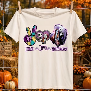 May include: A cream-colored t-shirt featuring a graphic design with the text PEACE LOVE NIGHTMARE. The design includes a peace sign, a heart containing Jack and Sally, and an illustration of the characters, all in purple, black, and yellow.