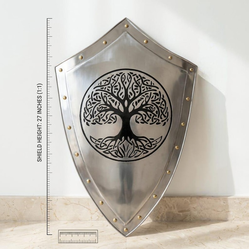 Pu&ograve; includere: Uno scudo in metallo color argento con un design circolare nero dell'albero della vita al centro. Lo scudo ha una base a punta ed &egrave; decorato con piccoli rivetti color ottone lungo i bordi. Un righello indica un'altezza di 68,58 cm.