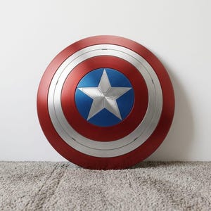 May include: A round shield with a red outer ring, a silver middle ring, and a blue center with a silver star. The shield is a replica of Captain America's shield.