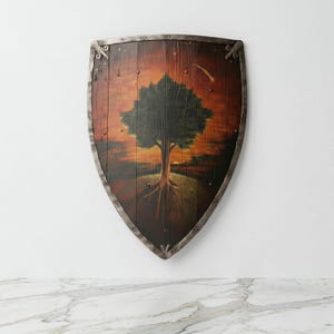 May include: A wooden shield with a metal frame. The shield displays a painting of a tree with visible roots set against a sunset background. The shield is mounted on a white wall.