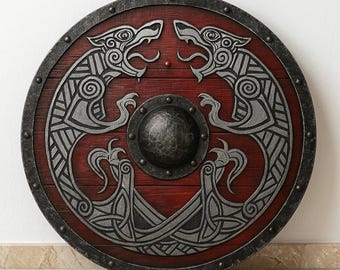 Può includere: Uno scudo circolare in legno con una finitura rosso scuro e un prominente umbone metallico centrale. La superficie è decorata con due figure di lupi stilizzate color argento che si fronteggiano, circondate da un bordo metallico scuro e usurato.