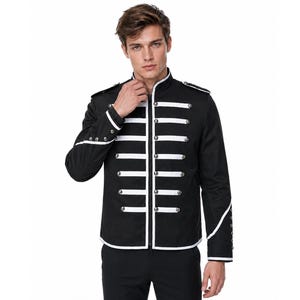 Könnte beinhalten: Eine schwarze Jacke im Militärstil mit Stehkragen, langen Ärmeln und einem Frontreißverschluss. Das Kleidungsstück ist mit horizontalen weißen Bändern und silberfarbenen Knöpfen verziert, die in Reihen auf der Brust und an den Ärmelbündchen angeordnet sind.