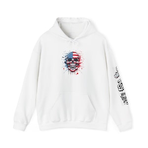 May include: White hoodie featuring a skull design with an American flag motif. The skull is split, with the left side displaying the stars and the right side displaying the stripes. The hoodie has a front pocket and text on the sleeve.