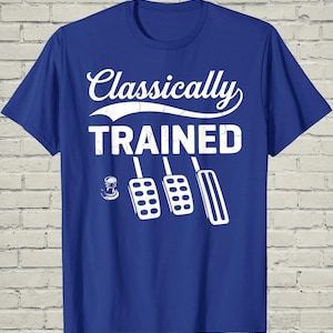 May include: A blue t-shirt with the words "Classically TRAINED" in white, along with a graphic of a clutch, brake, and accelerator pedals. The shirt has a crew neck and short sleeves.