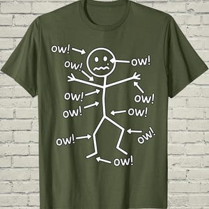 May include: Olive green t-shirt featuring a stick figure with arrows pointing to various body parts, each labeled with "ow!". The stick figure has a distressed expression, suggesting pain. A humorous design.