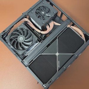May include: An overhead shot of a computer case with components installed. The case is dark gray and contains a power supply, two fans, and a graphics card labeled RTX 3080. The fans are black and gray, and the graphics card has a black mesh design.
