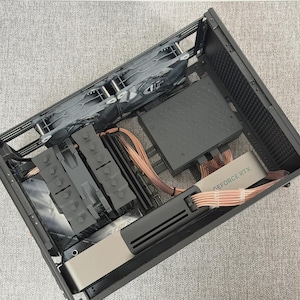 Könnte beinhalten: Ein offenes schwarzes Computergehäuse mit sichtbaren internen Komponenten. Enthält eine Grafikkarte mit der Aufschrift "GEFORCE RTX", ein Netzteil, Lüfter und verschiedene Kabel. Die Komponenten sind im Gehäuse angeordnet.