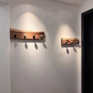 May include: Two wall-mounted coat racks made from natural live-edge wood planks. The larger rack features four smooth, rounded stone-like hooks, while the smaller rack features three matching stone-like hooks, all mounted horizontally.
