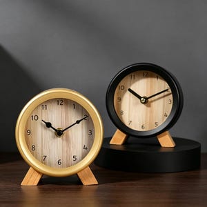 Peut inclure: Deux petites horloges analogiques rondes. L'une a un cadre doré et l'autre un cadre noir. Les deux ont des cadrans en bois clair avec des aiguilles et des chiffres noirs. Chaque horloge repose sur un petit support en bois.