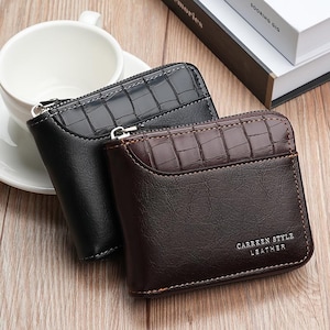 Puede incluir: Dos carteras plegables con cierre de cremallera, una en negro y otra en marrón oscuro. Ambas presentan una sección inferior lisa y un panel superior texturizado con patrón de cocodrilo. La cartera marrón tiene el texto CARRKEN STYLE LEATHER.