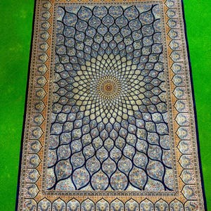 Puede incluir: Una alfombra rectangular que presenta un medall&oacute;n central con un patr&oacute;n floral radiante en tonos azul, crema y dorado. La alfombra tiene un borde azul oscuro con motivos repetitivos intrincados y flecos claros en los extremos superior e inferior.