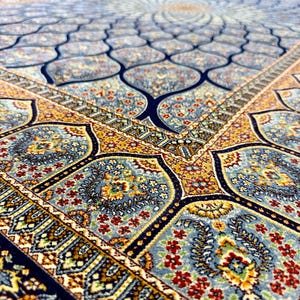 Puede incluir: Una alfombra rectangular con un complejo patr&oacute;n repetitivo de motivos florales en azul, dorado y rojo. El dise&ntilde;o incluye formas festoneadas interconectadas y bordes intrincados con elementos bot&aacute;nicos detallados en una textura densa.