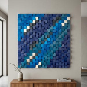 May include: A square wall art piece composed of numerous small, individual wooden blocks arranged in a grid. The blocks are painted in varying shades of blue, dark navy, and light teal, with some blocks featuring white accents to create a textured effect.