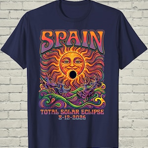 May include: A navy blue t-shirt featuring a colorful graphic of a sun with a face during a total solar eclipse. The design includes the text SPAIN, TOTAL SOLAR ECLIPSE, and 8-12-2026, surrounded by swirling patterns and figures in motion.