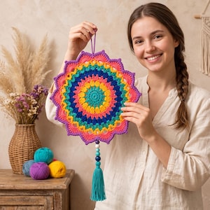 May include: A circular crochet wall hanging featuring a vibrant rainbow pattern with concentric rings of yellow, teal, blue, and pink. The piece is finished with a dangling string of colorful beads and a long teal tassel hanging from the bottom.