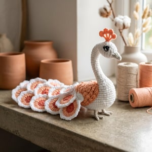 May include: A crocheted peacock figurine featuring a white body and neck with a peach-coloured crest and back. The tail consists of multiple circular, layered crochet motifs in white and peach. The eyes are embroidered in black thread.