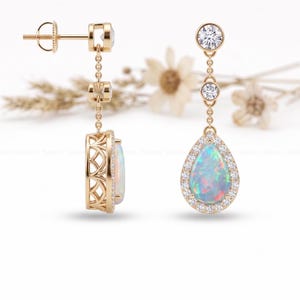 May include: Gold drop earrings with a pear-shaped opal gemstone surrounded by a halo of small, clear stones. The earrings have a delicate chain design with additional clear stones and a decorative filigree setting.