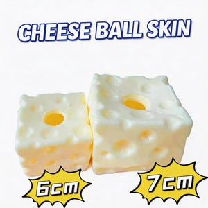 May include: Two off-white, cube-shaped objects with a textured surface resembling Swiss cheese, featuring multiple circular indentations. The text CHEESE BALL SKIN appears above, with 6cm and 7cm labels in yellow starbursts below each cube.
