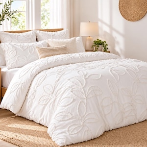 Puede incluir: Una funda nórdica blanca y fundas de almohada a juego con un patrón de hojas con relieve y textura. El juego de cama incluye un edredón blanco texturizado con un diseño botánico, junto con almohadas coordinadas que muestran el mismo motivo.