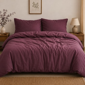 May include: A deep plum-coloured duvet cover set featuring a textured fabric finish. The bedding includes two matching rectangular pillow shams placed horizontally against the headboard, creating a uniform and solid-coloured appearance.