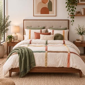 May include: A bed featuring a white duvet cover with a grid of tufted, multi-coloured textured lines in shades of sage green, terracotta, and mustard yellow. The bed includes a beige upholstered headboard, a sage green throw blanket, and pillows.
