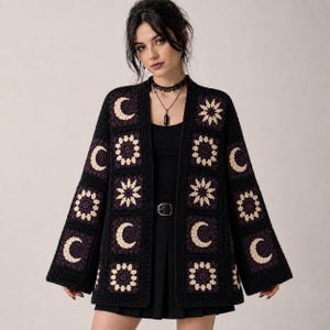 May include: A black crochet cardigan featuring a repeating pattern of cream-colored crescent moons and star-like floral motifs. The garment has an open front, long wide sleeves, and is constructed from square panels with a dark, textured yarn finish.