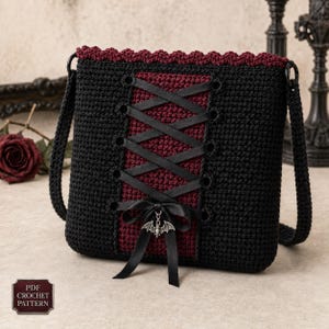 Può includere: Una borsa all'uncinetto nera e rosso scuro con un pannello centrale con lacci in nastro nero a incrocio. La borsa presenta un bordo superiore smerlato, un fiocco in nastro nero sul fondo e un ciondolo a forma di pipistrello. Testo: PDF CROCHET PATTERN.