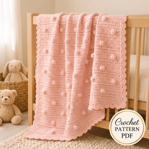 May include: A light pink crochet blanket featuring a textured bobble stitch pattern throughout the main body, finished with a scalloped edge border. A circular white badge in the corner displays the black text Crochet PATTERN PDF.