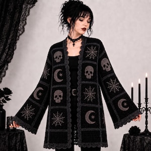 Puede incluir: Un cárdigan de ganchillo negro con un patrón repetitivo de calaveras, telarañas y lunas crecientes con estrellas. La prenda tiene mangas largas y anchas, y un borde gris festoneado a lo largo de la abertura frontal y el dobladillo.