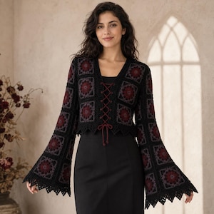 May include: A long-sleeved crochet cardigan constructed from black and dark red floral granny squares. The garment features a V-neckline with a central dark red lace-up closure, flared bell sleeves, and a scalloped hemline edge in black.