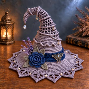 Puede incluir: Un sombrero puntiagudo de ganchillo color lavanda con ala ancha de borde festoneado y pequeñas cuentas blancas. El sombrero está decorado con una banda azul oscuro, una gran rosa de ganchillo azul oscuro, hojas verdes, un dije de mariposa y estrellas.