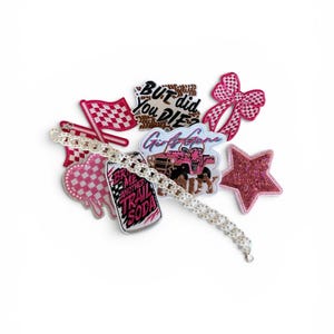 Puede incluir: Una colección de parches bordados que incluye una bandera a cuadros rosa, un corazón rosa, un lazo rosa, una estrella rosa brillante, un vehículo todoterreno rosa y un parche de lata con el texto BRING ME ANOTHER TRAIL SODA y BUT DID YOU DIE.