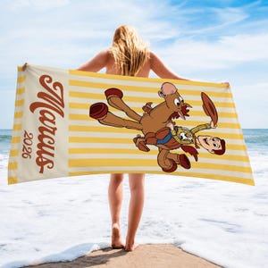 May include: A rectangular beach towel featuring a yellow and white striped pattern. The towel displays a cartoon illustration of a cowboy riding a brown horse, with the name Marcus and the year 2026 printed in a large, brown, cursive font on the left.