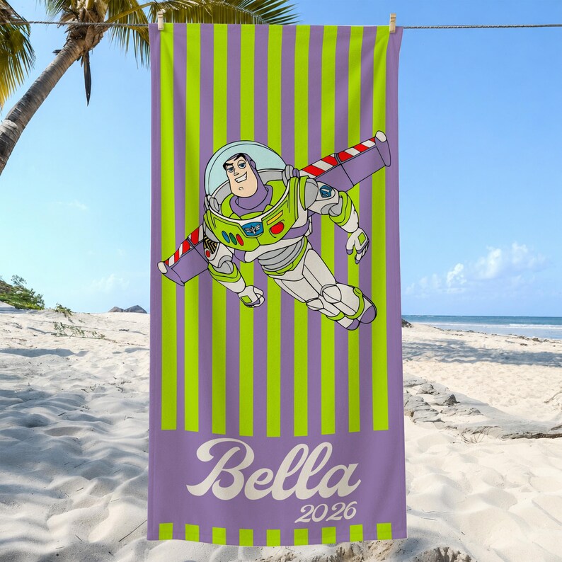 May include: A rectangular beach towel featuring a vertical lime green and purple striped pattern. The center displays a graphic of a space ranger character in a white, green, and purple suit. The name Bella and the year 2026 are printed in white.