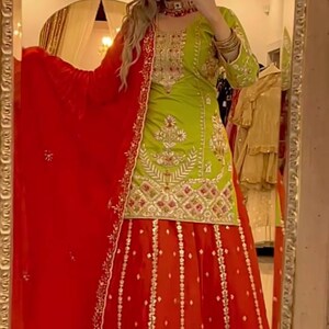 May include: A lime green tunic featuring intricate gold embroidery and sequin detailing, paired with a vibrant red floor-length skirt adorned with gold patterns and a matching red dupatta with an embroidered border and small gold accents.