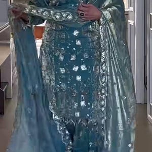 May include: A teal blue salwar kameez set featuring a long-sleeved tunic with silver metallic embroidery and square mirror embellishments. The outfit includes matching trousers and a coordinating sheer dupatta with a scalloped silver embroidered border.