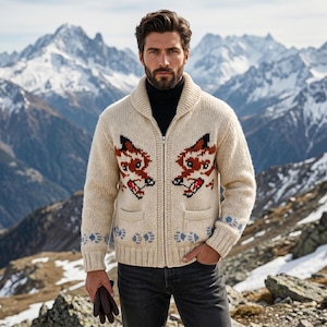Puede incluir: Cárdigan crema con cremallera, cuello chal y dos bolsillos delanteros. El cárdigan presenta un diseño de zorro repetido en marrón, negro y rojo. Acentos florales azules en los puños y el dobladillo. El fondo muestra una cordillera.