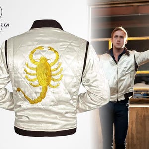 May include: A satin white jacket with a gold scorpion embroidered on the back. The jacket has a quilted pattern, black trim, and a brown collar. The Enviro Jackets logo is in the upper left corner. A person is wearing the jacket in the background.