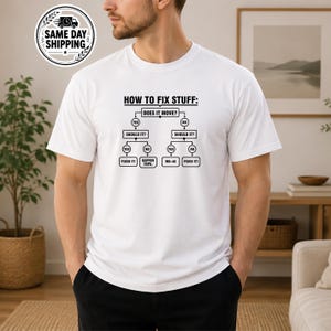 May include: A white short-sleeved t-shirt featuring a black graphic print of a flowchart titled HOW TO FIX STUFF. The diagram outlines decision paths with text boxes including DOES IT MOVE, SHOULD IT, FIXED IT, GAFFER TAPE, and WD-40.