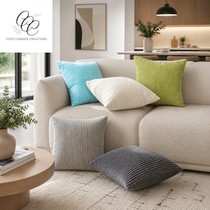 May include: A selection of corduroy cushions in shades of light blue, cream, lime green, grey, and charcoal. The cushions are displayed on a beige sofa and on the floor. A round wooden coffee table and a vase with greenery are also visible.