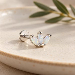 May include: A silver-toned metal labret piercing featuring a crown-shaped top set with three marquise-cut white opals. The jewelry has a flat circular back and a post, with the opal stones displaying iridescent flashes of color.