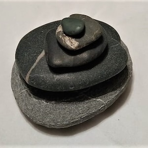 Puede incluir: Una pila de cinco piedras lisas, grises y verdes, equilibradas una encima de la otra.