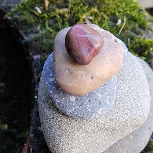 May include: A stack of grey stones with a red and white stone on top. The stones are arranged in a pyramid shape.