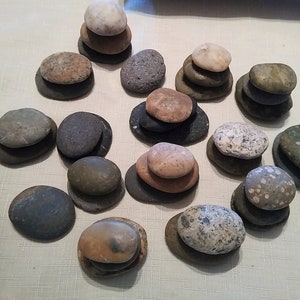 Puede incluir: Una colección de 14 pilas de piedras lisas, grises, marrones y blancas, cada pila está equilibrada una encima de la otra.