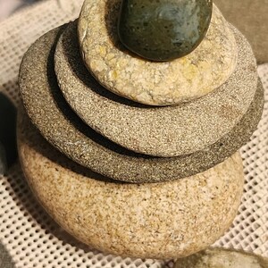 May include: A stack of smooth, grey and beige stones with a green stone on top. The stones are arranged in a pyramid shape.